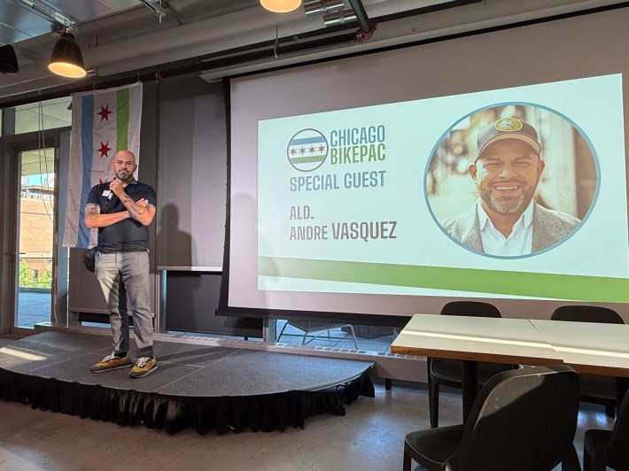 40th Ward Alderperson Andre Vasquez standing on a small stage in front of a presentation screen
